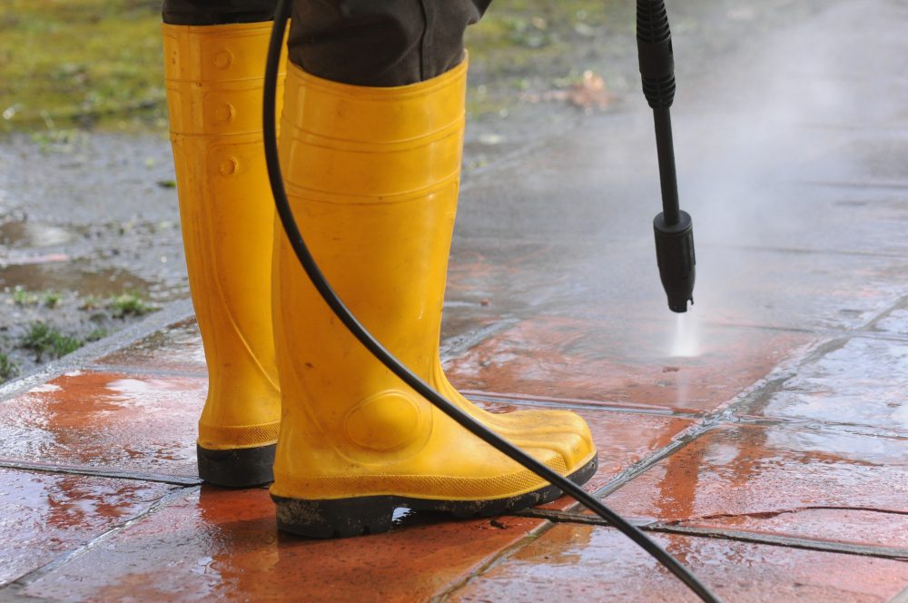 person wearing yellow rubber boots with high pressure water nozzle cleaning dirt tiles